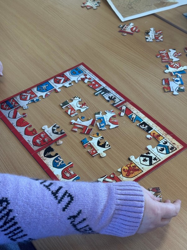 A jigsaw with the border complete and a hand adding some more jigsaw pieces to complete the centre of the puzzle